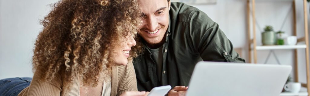 young smiling couple looking at computer to see how much they earned from online hustle.